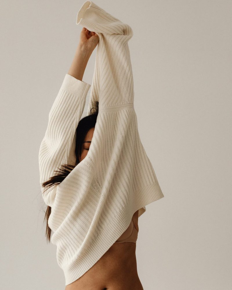 Femme à la peau matte et aux cheveux bruns longs, retirant son pull beige vers le haut laissant voir son ventre