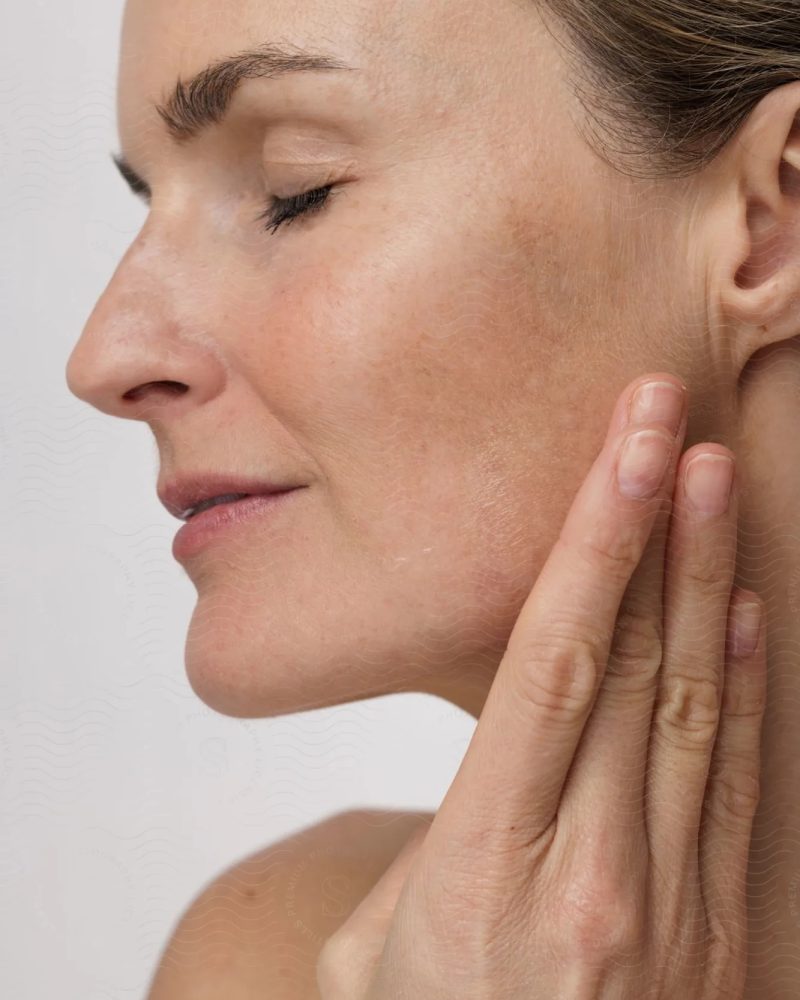 Femme d'âge mur vue de profil, cheveux attachés et se tenant le visage avec sa main