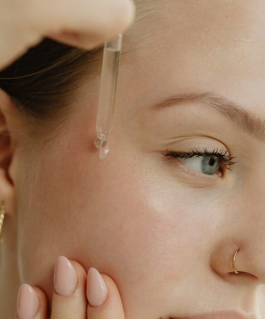 Gros plan sur le visage d'une femme appliquant du sérum sur sa pommette à l'aide d'une pipette