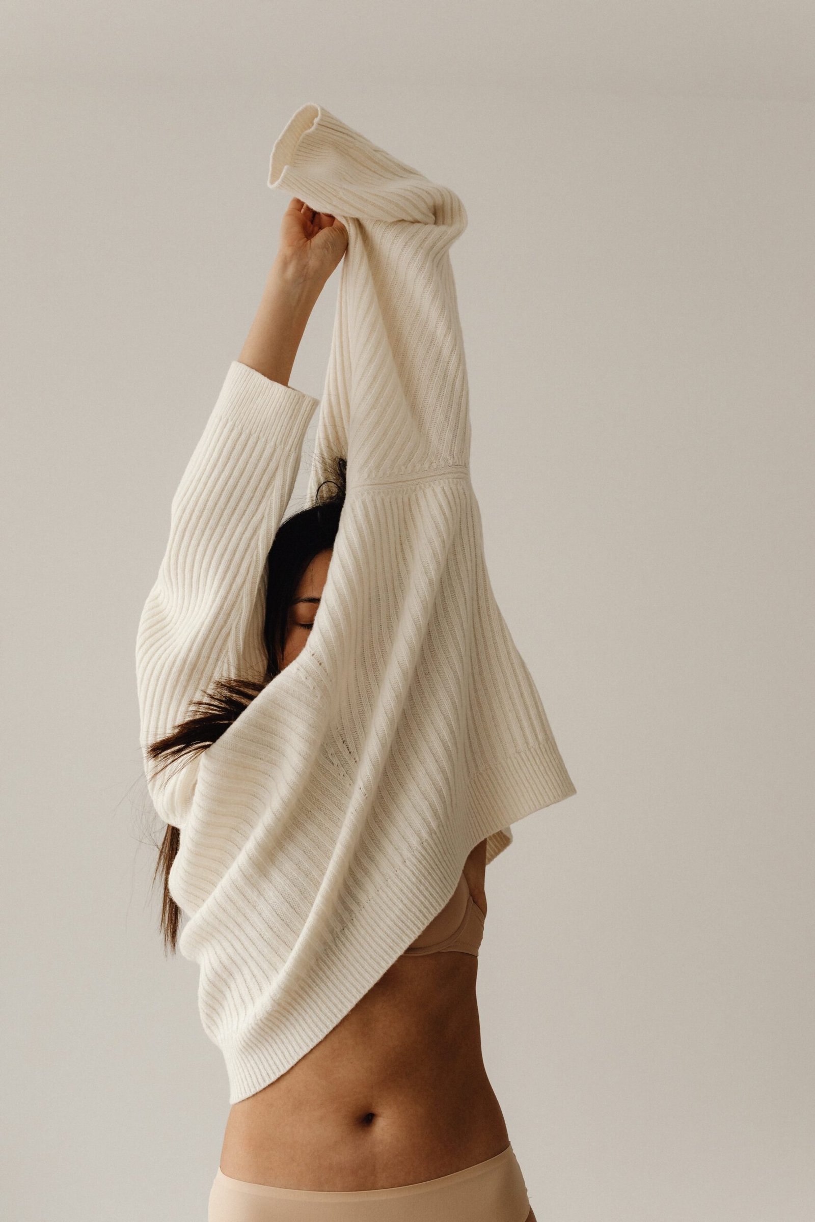 kaboompics_living-neutral-capturing-the-beauty-lifestyle-aesthetic-30688-min-scaled Femme à la peau matte et aux cheveux bruns longs, retirant son pull beige vers le haut laissant voir son ventre