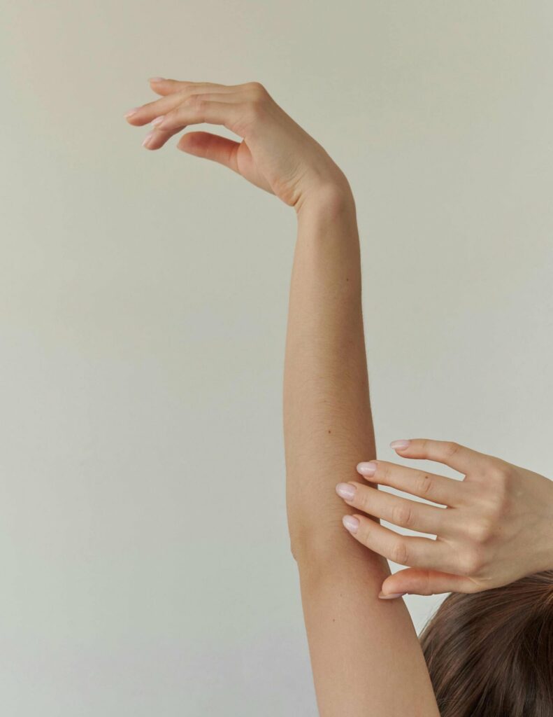 Femme brune avec les cheveux attachés en chignon, bras levés vers le haut ; la photo est coupé de sorte qu'on ne voit que le haut de tête de la femme et ses bras
